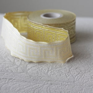 May include: A roll of yellow and white patterned trim with a geometric design. The trim is folded in half and the roll is visible.