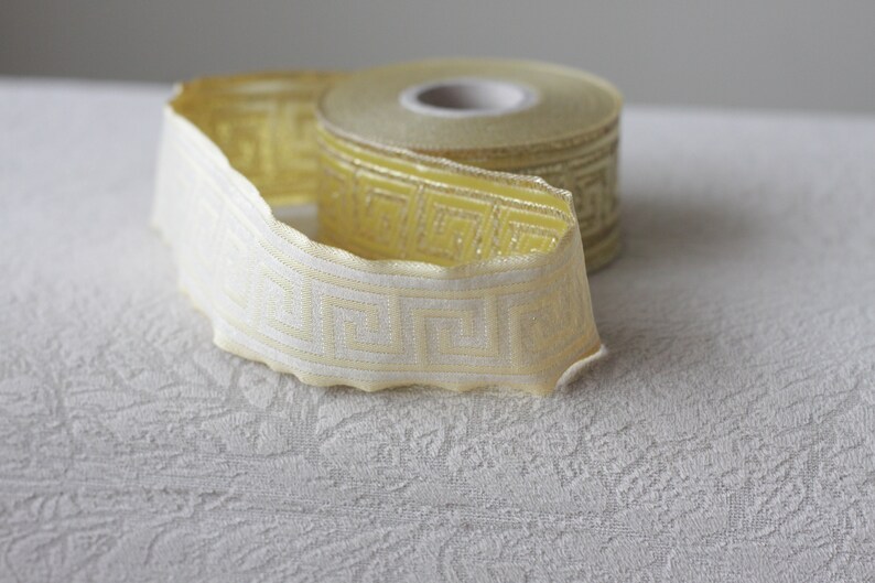 May include: A roll of yellow and white patterned trim with a geometric design. The trim is folded in half and the roll is visible.