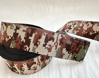May include: Camouflage patterned elastic ribbon in brown, green, and beige colors. The ribbon is rolled up and the pattern is visible on both sides.
