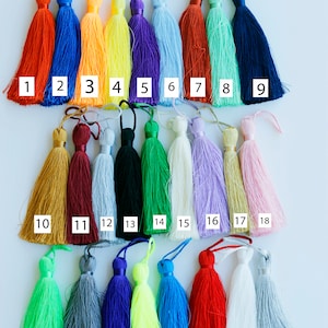 Könnte beinhalten: Sechsundzwanzig bunte Quasten in verschiedenen Farben, darunter Rot, Orange, Gelb, Grün, Blau, Lila, Rosa, Weiß, Schwarz und Grau. Die Quasten sind von 1 bis 26 nummeriert.