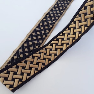 May include: Two decorative ribbons with a woven pattern. One ribbon is black with a gold woven design, and the other is gold with a black woven design. The ribbons are on a white background.