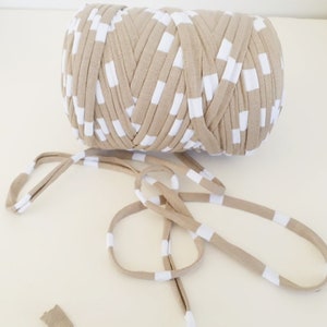 May include: A roll of beige and white striped yarn with white squares. The yarn is made of soft, stretchy fabric and is perfect for crocheting or knitting.