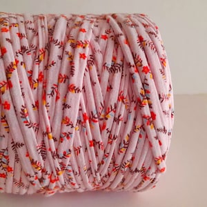 May include: A roll of pink cotton yarn with a floral print. The yarn is made from recycled fabric and is ideal for crocheting or knitting.