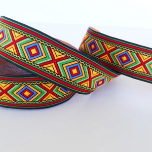 May include: A roll of black and red trim with a colorful geometric pattern featuring yellow, green, blue, and red squares. The trim is woven with a repeating pattern of diamonds and crosses.