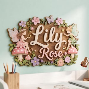 May include: A wooden wall plaque featuring the name Lily Rose in raised cream lettering. The design includes two fairies with wings, pink and purple flowers, green leaves, a butterfly, and two red mushrooms with white spots on a dark wood base.