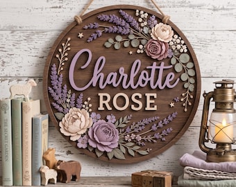 以下が含まれることがあります： Charlotte ROSEという名前が浮き彫りになった円形の木製ウォールサイン。紫、ラベンダー、クリーム色の立体的なフラワーアレンジメントで装飾されており、小さな木製の星や葉のモチーフがアクセントになっています。