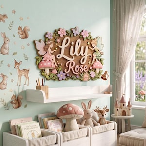 May include: A wooden wall sign featuring the name Lily Rose in raised white lettering, surrounded by sculpted fairies, pink mushrooms, and flowers. The wall is decorated with decals of rabbits, squirrels, and a deer, with books and plush toys below.