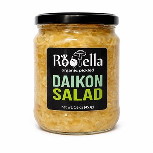 May include: A clear glass jar filled with organic pickled daikon salad. The jar has a black lid and a black label with white and green text that reads "Röella organic pickled DAIKON SALAD" and "net wt. 16 oz (453g)".