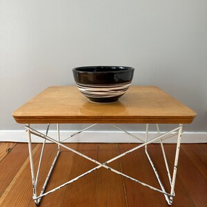 May include: A black and white striped ceramic bowl sits on a wooden table with a white metal frame.