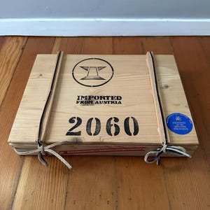 May include: A wooden crate with a black and white logo that says "IMPORTED FROM AUSTRIA" and the number "2060". The crate has a blue and white sticker that says "PREMIERT 1998, DIPLOME D'HONNEUR".
