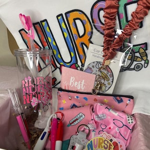 May include: A gift box filled with nurse-themed items. Includes a white tote bag with the word "NURSE" in colorful letters, a clear tumbler, pink accessories, pens, keychains, and stickers. A lanyard is also included.