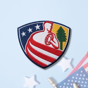 May include: A shield-shaped embroidered patch featuring a white silhouette of a person holding a football, wrapped in red and white stripes. The background includes three white stars on a blue field and a green pine tree on a yellow field.