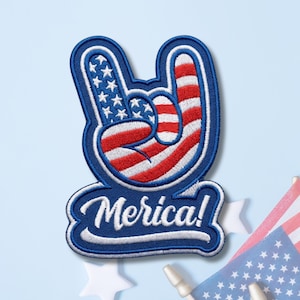 May include: An embroidered patch shaped like a hand making a rock-and-roll gesture. The hand features a red, white, and blue American flag pattern. Below the hand, a dark blue banner contains the white embroidered text Merica! in a script font.