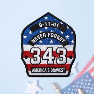 May include: A shield-shaped embroidered patch featuring the American flag, the text 9-11-01, NEVER FORGET, 343, and AMERICA'S BRAVEST. The design includes a blue field with white stars, white and red stripes, and black borders with white lettering.
