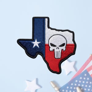 May include: An embroidered patch in the shape of the state of Texas featuring the Texas flag design with a blue vertical stripe containing a white star, followed by white and red horizontal stripes with a white skull graphic centered on them.
