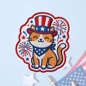 May include: An embroidered patch featuring an orange and white cat wearing a red, white, and blue top hat and a matching bandana. The cat is surrounded by red and blue firework bursts and small stars, all outlined in a thick red border.