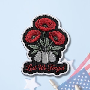 May include: An embroidered patch featuring three vibrant red poppy flowers with green leaves above three silver-toned military dog tags. The black background is bordered in white, and the text "Lest We Forget" is stitched in red at the bottom.