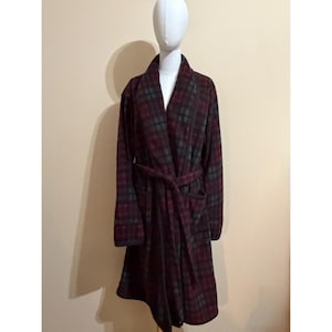 May include: A long-sleeved robe featuring a dark red, black, and forest green plaid pattern. The garment includes a shawl collar, a matching fabric tie belt at the waist, and two front patch pockets. The robe is displayed on a white mannequin.