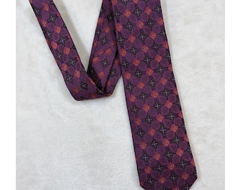 Könnte beinhalten: Eine violette Krawatte mit einem sich wiederholenden geometrischen Muster aus stilisierten vierblättrigen Blumenformen in dunklen Violett-, Schwarz- und Orangetönen. Der Stoff hat eine glatte Textur und die Krawatte ist gefaltet.