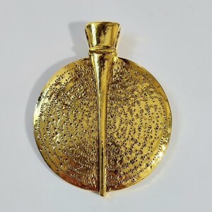 May include: A gold-colored pendant with a textured, circular design. The pendant has a central vertical element and a decorative top. The surface is covered in small, irregular perforations, giving it a unique appearance.