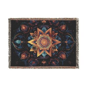 May include: A rectangular woven throw blanket featuring a dark black background with a central golden star-shaped mandala design. The pattern includes intricate blue and orange floral-like motifs surrounding the center, finished with fringed edges.