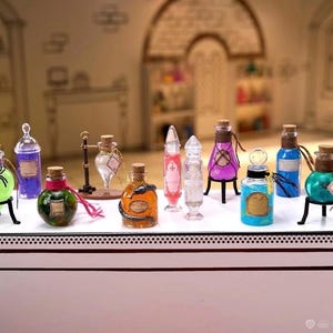 May include: A collection of miniature glass bottles filled with colorful liquids, including green, purple, orange, and blue, some featuring cork stoppers, small labels, and decorative elements like a spider or snake, with one pink heart-shaped bottle held up.