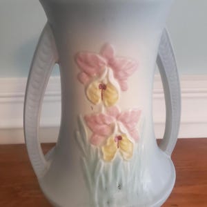 May include: A white ceramic mug with a black handle and the text "But First, Coffee" in a bold, black font. The mug is filled with a dark liquid, likely coffee, and sits on a white surface.