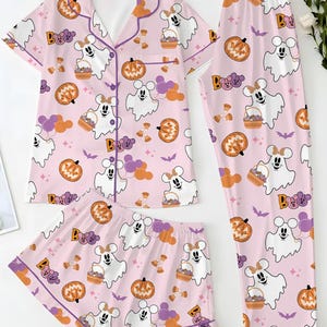 Peut inclure: Un ensemble de pyjama rose clair composé d'une chemise à manches courtes boutonnée, d'un short et d'un pantalon. Le tissu présente un motif répétitif de fantômes blancs avec des oreilles de souris, de citrouilles orange et le mot BOO.