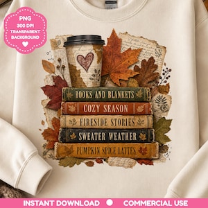 May include: A cream-coloured sweatshirt featuring a graphic of a stack of five books titled Books and Blankets, Cozy Season, Fireside Stories, Sweater Weather, and Pumpkin Spice Lattes, topped with a coffee cup and surrounded by autumn leaves.