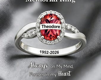 Puede incluir: Un anillo conmemorativo de tono plateado con una piedra central roja de forma ovalada con el nombre Theodore impreso. La piedra está rodeada por un halo de pequeñas piedras claras. El anillo tiene grabadas las fechas 1952-2026 y Memorial Ring.