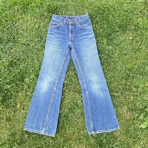 May include: A pair of blue denim jeans featuring a high-waisted design, a classic five-pocket construction, a metal button and zipper fly closure, and a straight-leg cut with subtle fading along the thighs and knees for a worn-in appearance.