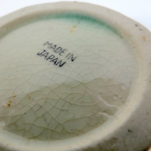 May include: Close-up of the bottom of a white ceramic object with a green glaze. The bottom has a crackled glaze and the words "Made in Japan" are printed in black.