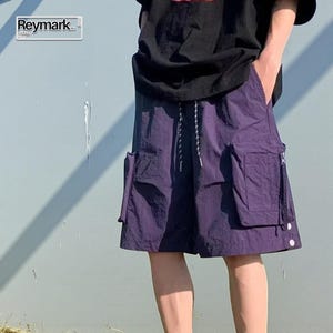 Multi Pocket Cargo Shorts | Men Baggy Streetwear Shorts | Casual Summer Outfit | Oversized Hip Hop Shorts | Gift for Him
.
Person wearing loose-fit black cargo shorts with multiple flap and zipper pockets, standing outdoors on a grassy field under a clear sky.