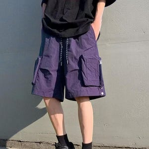 Multi Pocket Cargo Shorts | Men Baggy Streetwear Shorts | Casual Summer Outfit | Oversized Hip Hop Shorts | Gift for Him
.
Person wearing loose-fit black cargo shorts with multiple flap and zipper pockets, standing outdoors on a grassy field under a clear sky.