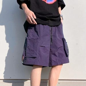 Multi Pocket Cargo Shorts | Men Baggy Streetwear Shorts | Casual Summer Outfit | Oversized Hip Hop Shorts | Gift for Him
.
Person wearing loose-fit black cargo shorts with multiple flap and zipper pockets, standing outdoors on a grassy field under a clear sky.