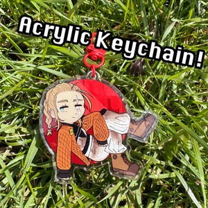 Könnte beinhalten: Acryl-Schlüsselanhänger mit einem Anime-Charakter mit blonden Haaren, der einen orangefarbenen Pullover und eine weiße Hose trägt. Der Schlüsselanhänger hat einen roten Hintergrund und einen roten Verschluss. Der Text "Acrylic Keychain!" ist in Weiß dargestellt.