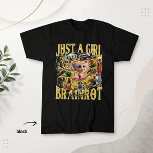 May include: A black short-sleeve t-shirt featuring a graphic print with the text "JUST A GIRL WHO LOVE BRAINROT" in yellow. The design includes a central character with a coffee cup head surrounded by various surreal, colourful figures.