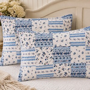 May include: Two rectangular quilted pillow shams featuring a patchwork design of alternating blue and white floral patterns and blue striped bands. The fabric displays a repeating grid of squares with stitched diamond quilting throughout the surface.