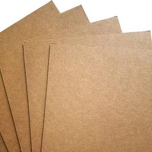 May include: A stack of five rectangular sheets of brown kraft paper board. Each sheet features a flat, matte, and textured surface with a consistent light brown color throughout. The sheets are arranged in a slightly fanned, overlapping formation.