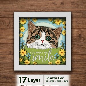 May include: A framed 17-layer shadow box art piece with a cat's face, green eyes, yellow flowers, and the text "You make me smile." The background is blue. The artwork is a decorative item.