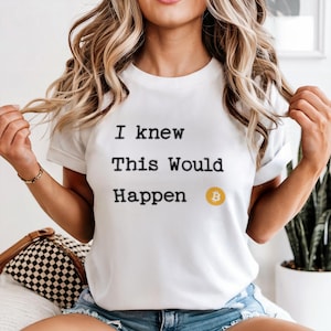 May include: White t-shirt with the text "I knew This Would Happen" in black, and a gold Bitcoin symbol. The shirt is a crew neck style.