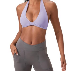 Puede incluir: Un sujetador deportivo lavanda con cuello halter y detalle frontal retorcido. Se combina con leggings grises con bolsillos. El conjunto está diseñado para actividades deportivas y ofrece un aspecto elegante y moderno.