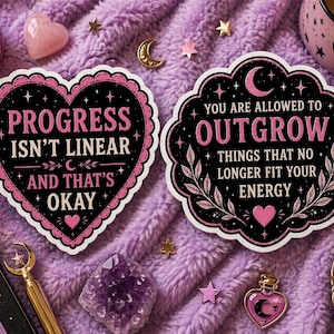 Puede incluir: Dos pegatinas decorativas con citas inspiradoras sobre un fondo morado. Una pegatina tiene forma de corazón y dice "PROGRESS ISN'T LINEAR AND THAT'S OKAY." La otra dice "YOU ARE ALLOWED TO OUTGROW THINGS THAT NO LONGER FIT YOUR ENERGY."