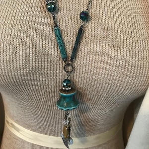 May include: A teal blue and silver necklace with a ceramic pendant, beads, and a charm with wings.