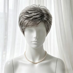 May include: A short, layered wig in shades of gray and brown is displayed on a mannequin. The wig has a natural-looking texture and a side-swept style. A delicate pearl necklace adorns the mannequin's neck, set against a white backdrop.