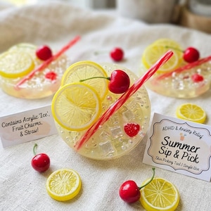 May include: Round, translucent resin discs embedded with yellow lemon slices, red cherries, and clear acrylic ice cubes, each featuring a red and white striped straw. Two white cards are present, one reading 'Contains Acrylic 'Ice', Fruit Charms, & Straw!' and the other 'ADHD & Anxiety Relief Summer Sip & Pick Skin Picking Tool | Single Use'.