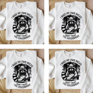 May include: White sweatshirt with a black and white graphic of a raccoon holding bread. The text "I BAKE MY OWN BREAD" and "DON'T TRUST THE GOVERNMENT" are printed on the shirt. The design is repeated on four sweatshirts.