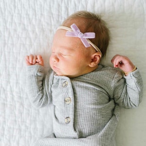 Puede incluir: Un bebé durmiendo con un mono gris de canalé con botones y una diadema de lazo lavanda.