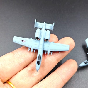 May include: A light blue model airplane with detailed wings, engines, and a cockpit. The miniature aircraft features a star emblem on the wing. The toy plane is a collectible item.