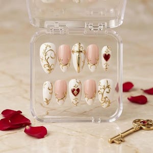 May include: A set of ten press-on nails in a clear plastic case, featuring a white and nude base with gold filigree accents. The designs include a gold sword emblem, red heart motifs with gold detailing, and intricate swirling gold patterns.